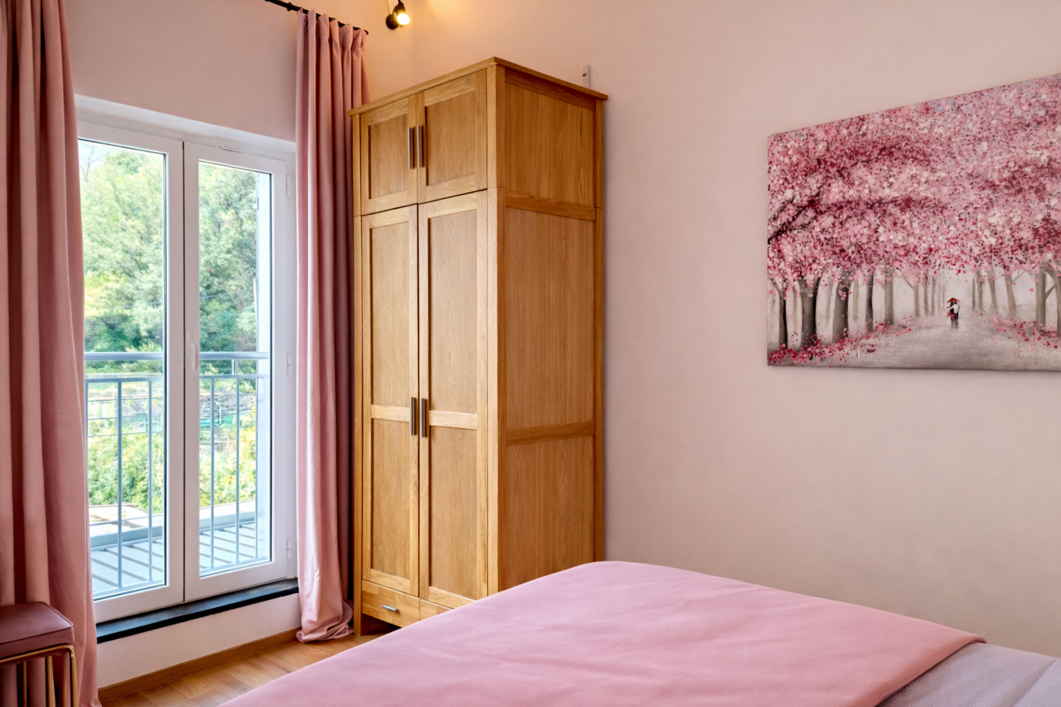 Bedroom with wooden wardrobe, pink bedspread and balcony windows.